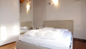 A bedroom with a bed, a nightstand, a mirror, and a wall-mounted light fixture.