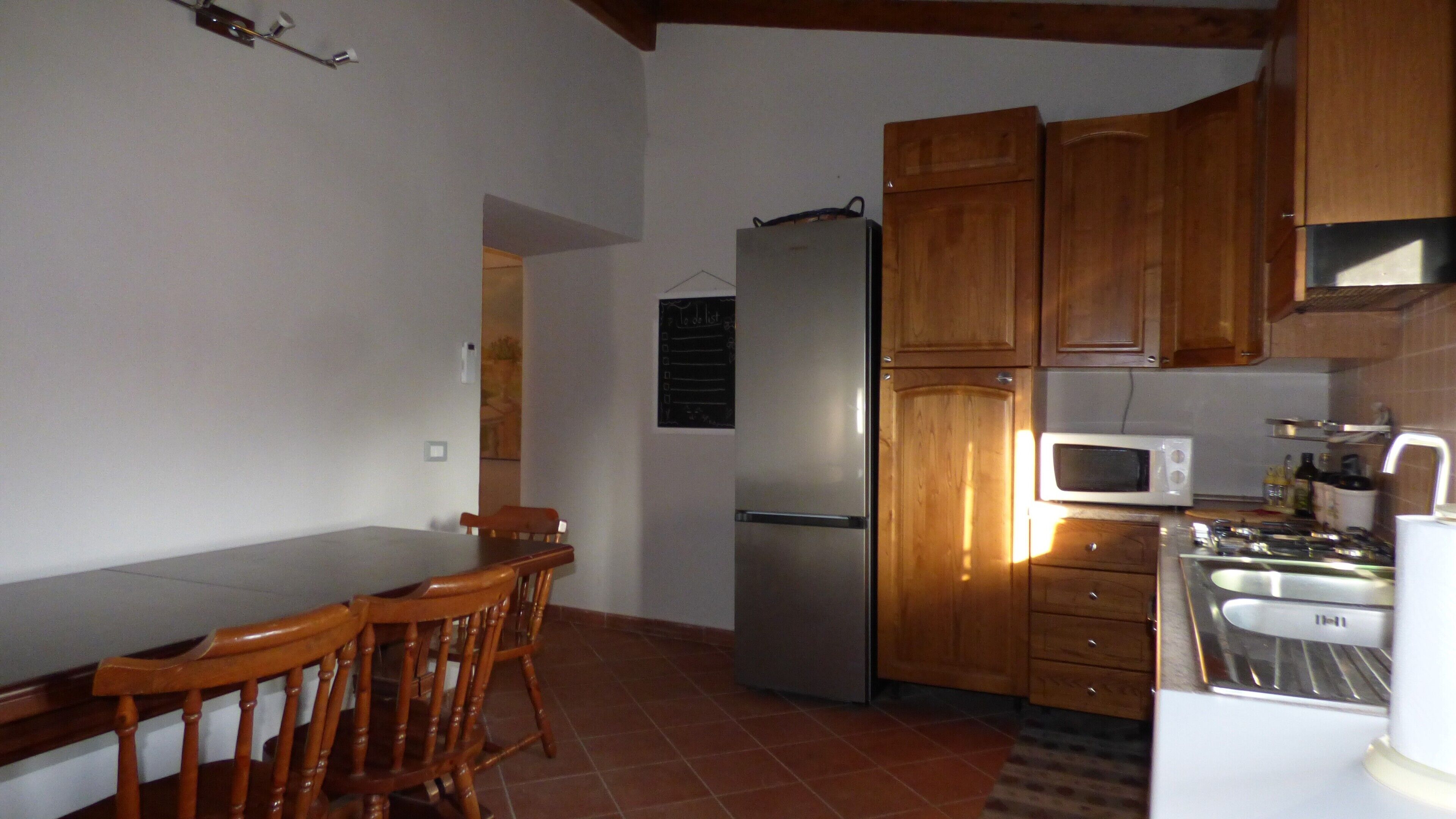A kitchen with wooden cabinets, a refrigerator, a microwave, and a dining table with chairs.