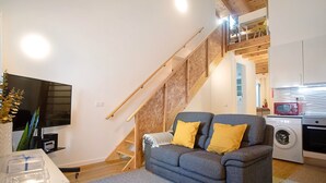 Un salon avec un canapé gris, un escalier en bois et un lave-linge.