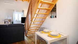 Une pièce de style loft avec un plafond en bois, une table à manger avec des sets de table jaunes, un canapé gris et un escalier.