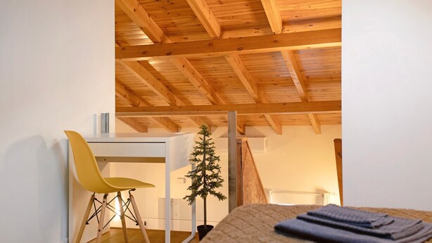 Une pièce avec un plafond en bois, un bureau blanc, une chaise jaune et un petit sapin de Noël.