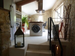 Une cuisine dotée d’un îlot central, d’une horloge et d’un escalier menant à un autre niveau.
