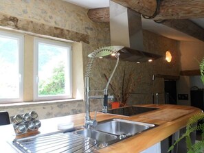 A kitchen with a wooden countertop, a stainless steel sink, and a stone wall.
