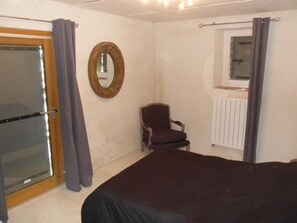 Ein Schlafzimmer mit einem Bett, einem Sessel, einem Fenster mit Vorhängen, einer Heizung und einem Spiegel an der Wand.