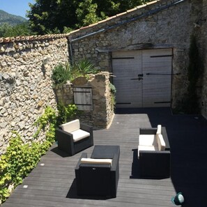 Un mur de pierre, deux portes et du mobilier d’extérieur sur une terrasse en bois.