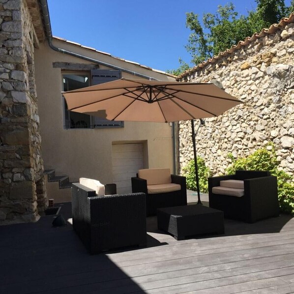 Eine Terrasse im Freien mit Korbmöbeln, einem großen Sonnenschirm und einer Steinmauer.