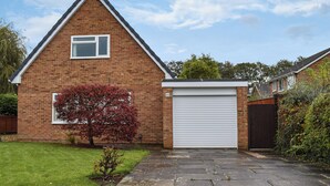 Une maison en briques avec une porte de garage, une petite fenêtre et un arbre aux feuilles rouges dans le jardin.