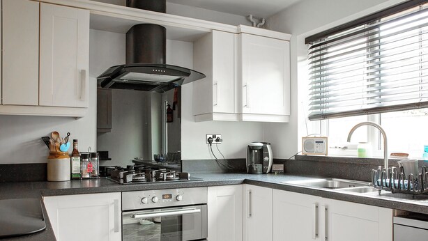 Une cuisine moderne avec des armoires blanches, une cuisinière en acier inoxydable et un four encastré.