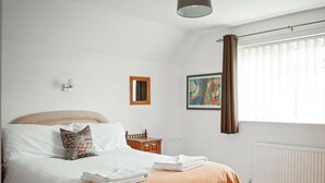 Un dormitorio con cama, una mesita de noche, un radiador, una ventana con cortinas, una lámpara de pared y un cuadro enmarcado.