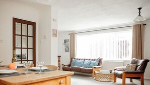 Un salón espacioso con una mesa de comedor de madera, un sofá de cuero marrón y un sillón de cuero marrón, además de un ventanal con cortinas.