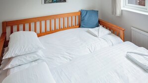 Un lit bien fait, avec du linge de lit blanc et une tête de lit en bois.