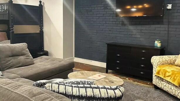 A modern living room with a large sectional sofa, a black headboard bed, a flat-screen TV mounted on a brick wall, and a small side table. - Downtown Studio loft in Rome.

 (Rome)