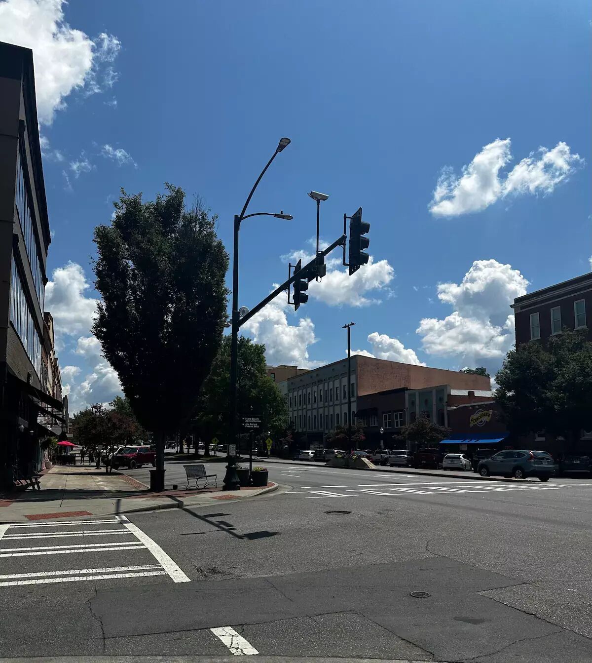 Una intersección de calles con semáforos, un paso de peatones y edificios al fondo.