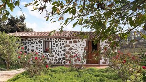 Ein Haus mit Steinaußenwand und Ziegeldach, umgeben von einem Garten mit verschiedenen Pflanzen und Blumen.