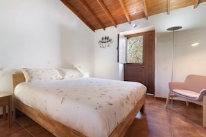 A bedroom with a wooden bed, a chair, a wardrobe, and a window with a view.
