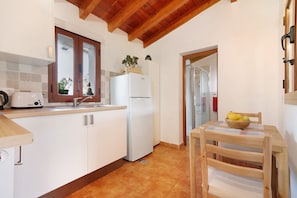 A kitchen with white cabinets, a white refrigerator, a wooden ceiling, and a table with a bowl of fruit.