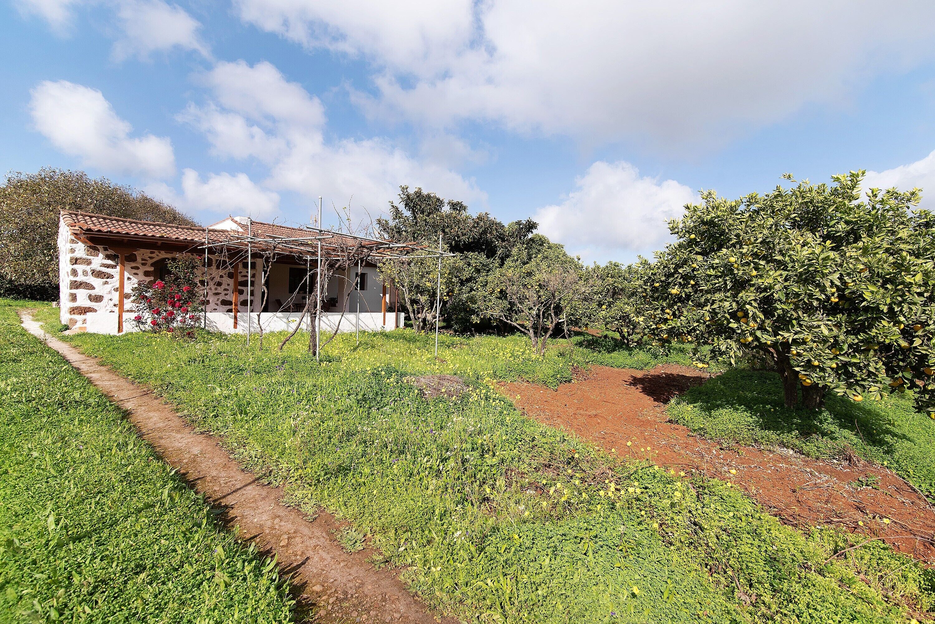 Un bâtiment en pierre avec un toit en tuiles, entouré de verdure et sous un ciel dégagé.