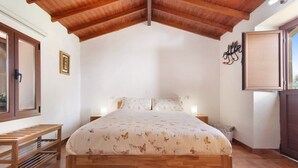 Ein Schlafzimmer mit einem hölzernen Bett, einer Sitzbank, einem Fenster und einer Tür.