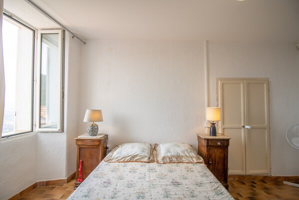 Une chambre à coucher avec un lit, deux tables de chevet avec des lampes, une armoire et une fenêtre.