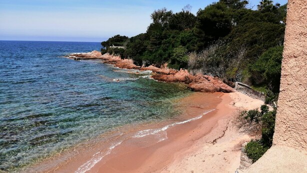 Una playa costera con agua cristalina, acantilados rocosos y abundante vegetación.