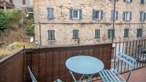 Un balcón con una mesa y sillas azules, con vistas a un edificio de piedra con contraventanas verdes.