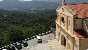 Un edificio con tejado de tejas rojas, una torre de campanas y vistas a un valle con montañas al fondo.