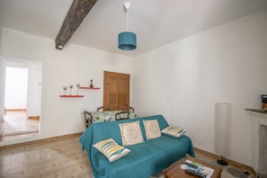 Une chambre à coucher avec un lit, une porte en bois, une étagère rouge, une table recouverte d’une nappe et une lampe.