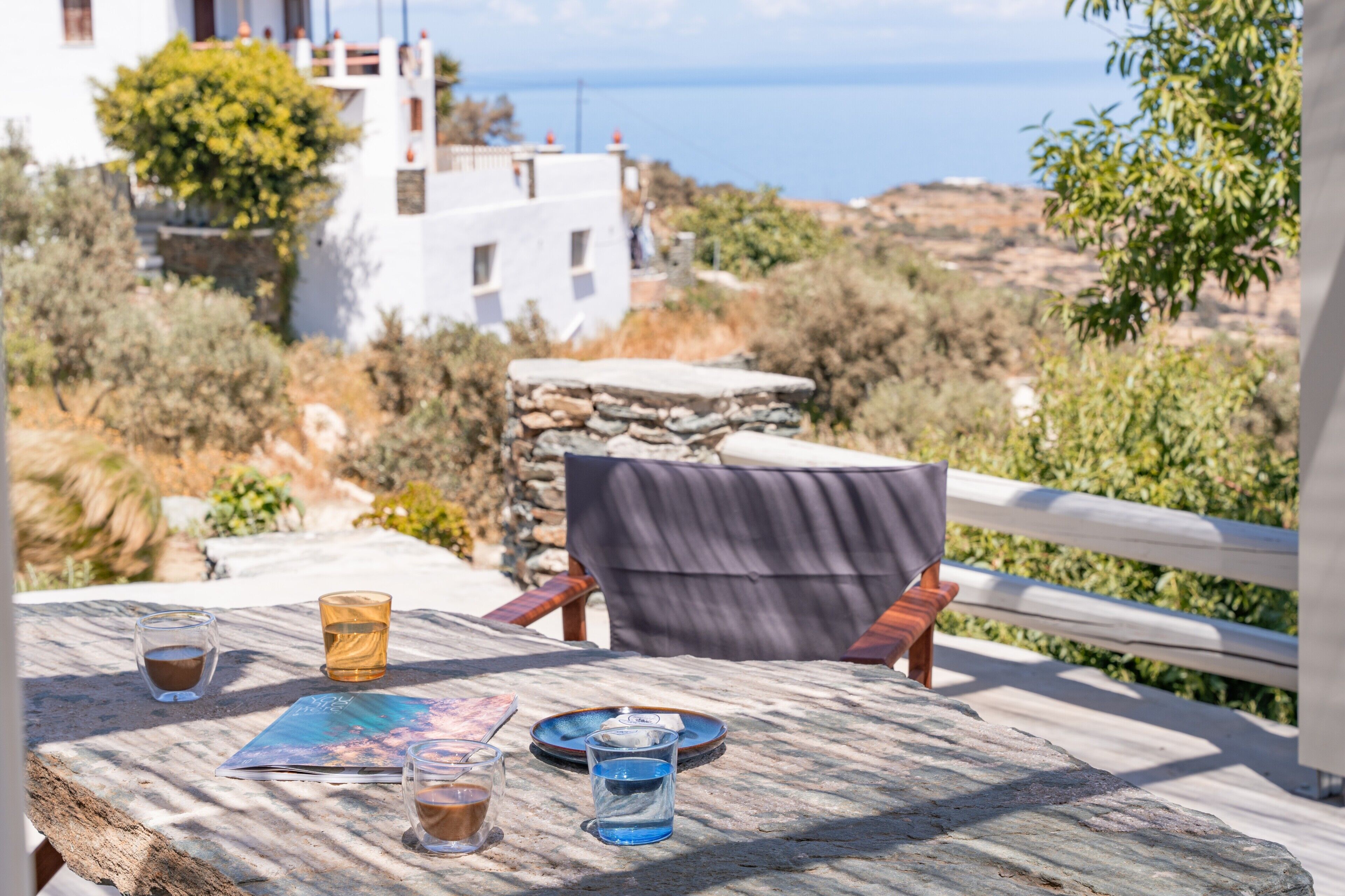 A table with drinks and a menu, a chair, and a view of the sea and buildings.