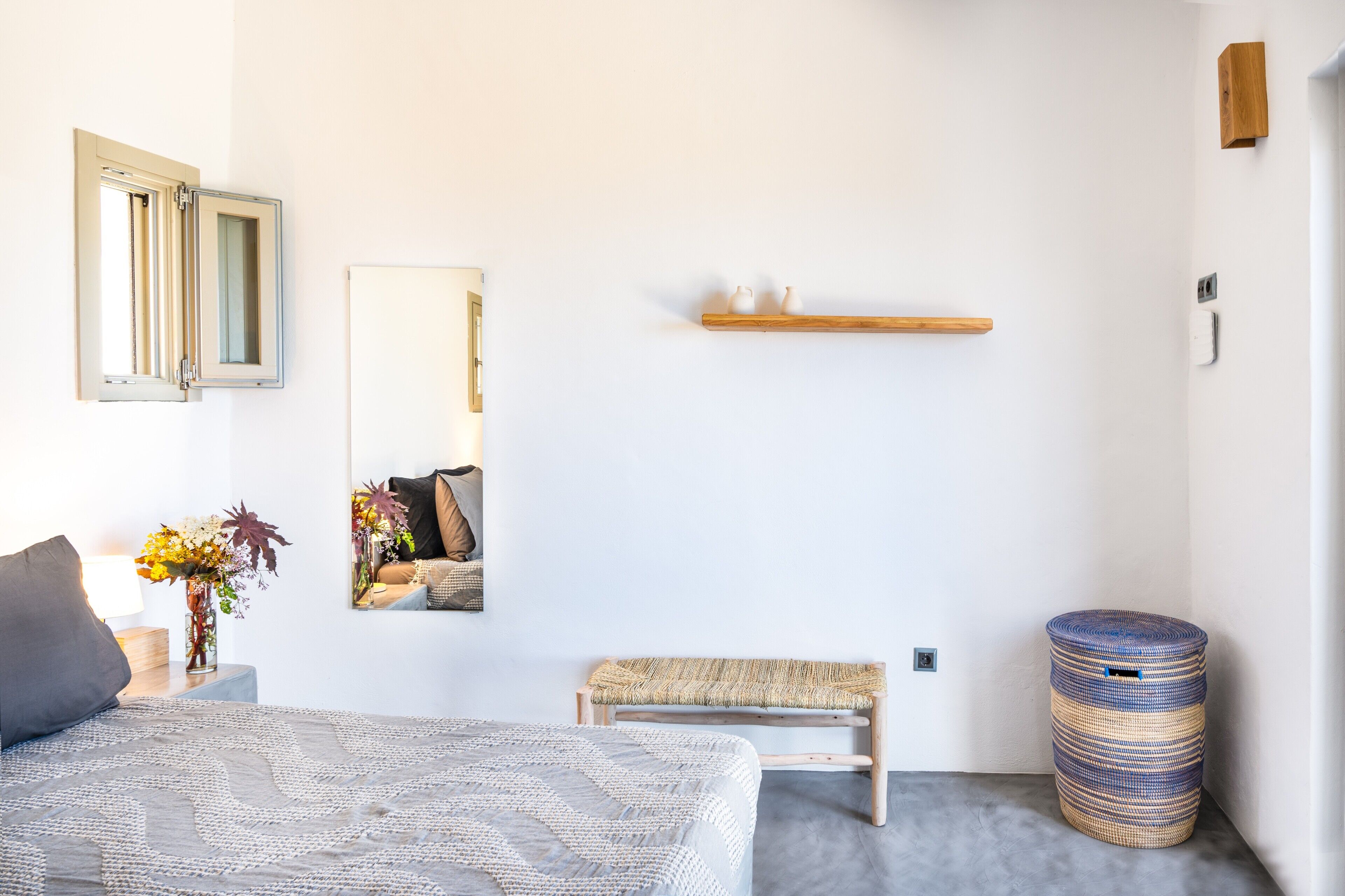 Un dormitorio con cama, una banca, un espejo, una estantería y un cubo de basura.