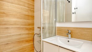 Ein Badezimmer mit Holzwand, einer Duschkabine aus Glas, einem weißen Waschbecken und einem Spiegel.