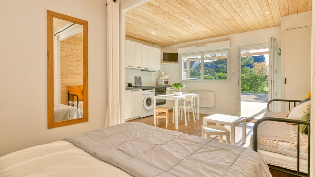 Ein Schlafzimmer mit Bett, Schreibtisch, Stuhl, einer Waschmaschine und Blick ins Freie.