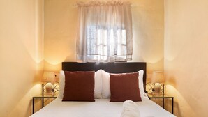 Un lit bien fait, avec une couette blanche, deux oreillers marron et une serviette blanche enroulée posée sur le lit.