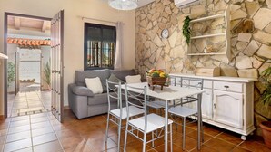 Un salon comprenant un canapé, des fauteuils, une table, un meuble blanc et un mur en pierre.