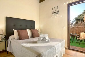 Une chambre à coucher avec un lit, des oreillers, une table de chevet et une vue sur un patio extérieur.