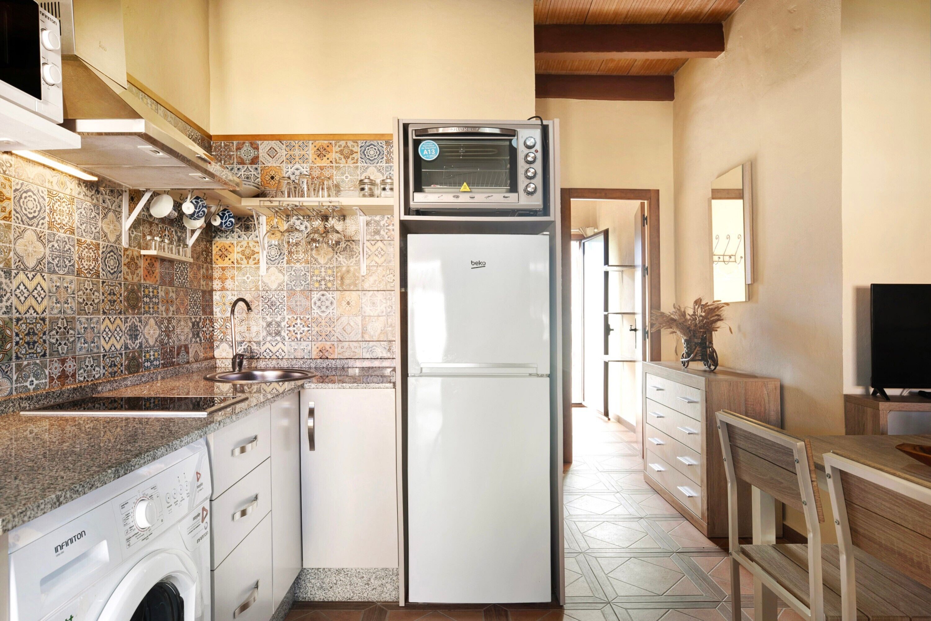 A compact kitchen with a built-in oven, a washing machine, and a refrigerator.
