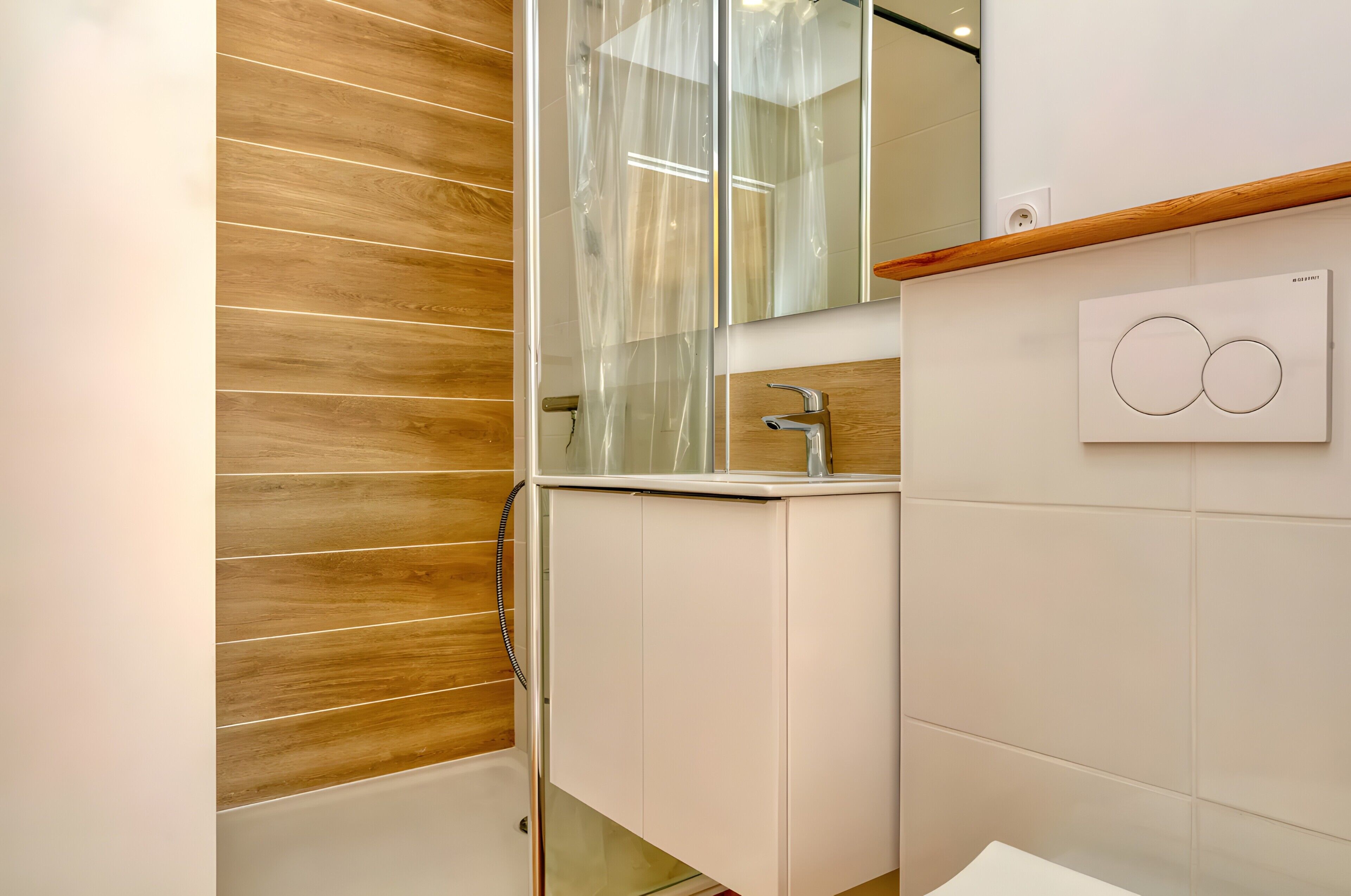 A bathroom with a wooden wall, a glass shower enclosure, a white sink, and a mirror.