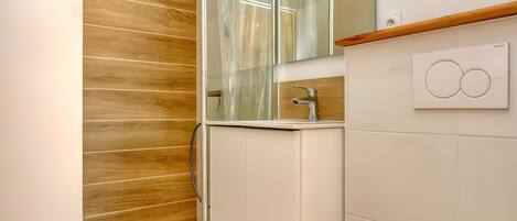 A bathroom with a wooden wall, a glass shower enclosure, a white sink, and a mirror.