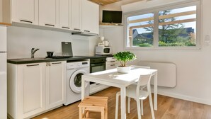 Una cocina moderna con armarios blancos, lavadora, una mesa de comedor con sillas y una ventana con vistas a zonas verdes.