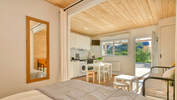 Un dormitorio con cama, escritorio, silla, lavadora y vistas al exterior.