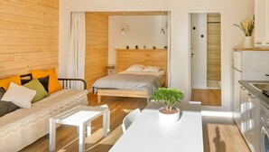 Una habitación moderna con techo de madera, una cama, una mesa blanca y una zona de cocina.