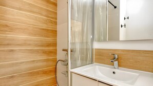 Un baño moderno con pared de madera, cabina de ducha de vidrio y lavamanos blanco.