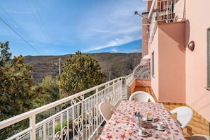 A balcony with a table set for two, overlooking a mountainous landscape.