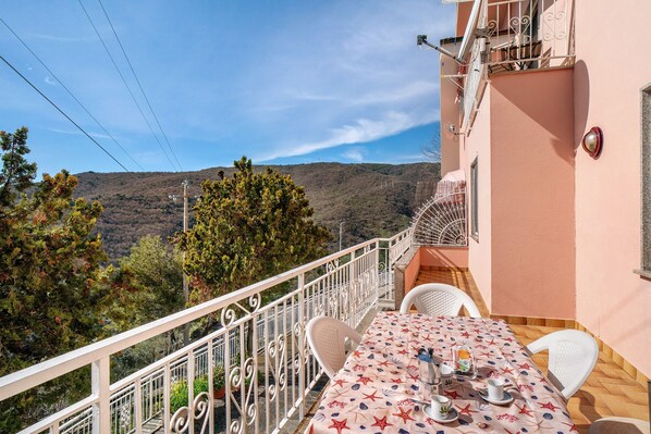 A balcony with a table set for two, overlooking a mountainous landscape.