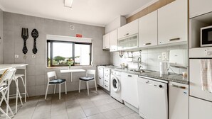 A modern kitchen with white cabinetry, a washing machine, a microwave, and a dining area with chairs and a table. - Villa 'Sublime Sun and Van, By Meco Stays' with Balcony and Wi-Fi (Alfarim)