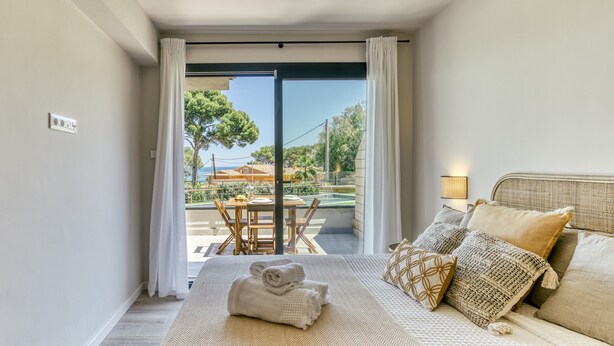 A bedroom with a bed, pillows, a bedside table, and a view of an outdoor patio. - Apartment 'Bonavista Begur' with Sea View, Wi-Fi and Air Conditioning (BEGUR)
