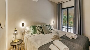 A neatly made bed with pillows and a blanket, a bedside lamp, and a window with curtains. - Apartment 'Bonavista Begur' with Sea View, Wi-Fi and Air Conditioning (BEGUR)