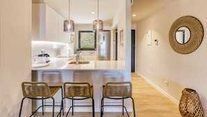 A modern kitchen with a central island, pendant lighting, and wicker chairs. - Apartment 'Bonavista Begur' with Sea View, Wi-Fi and Air Conditioning (BEGUR)