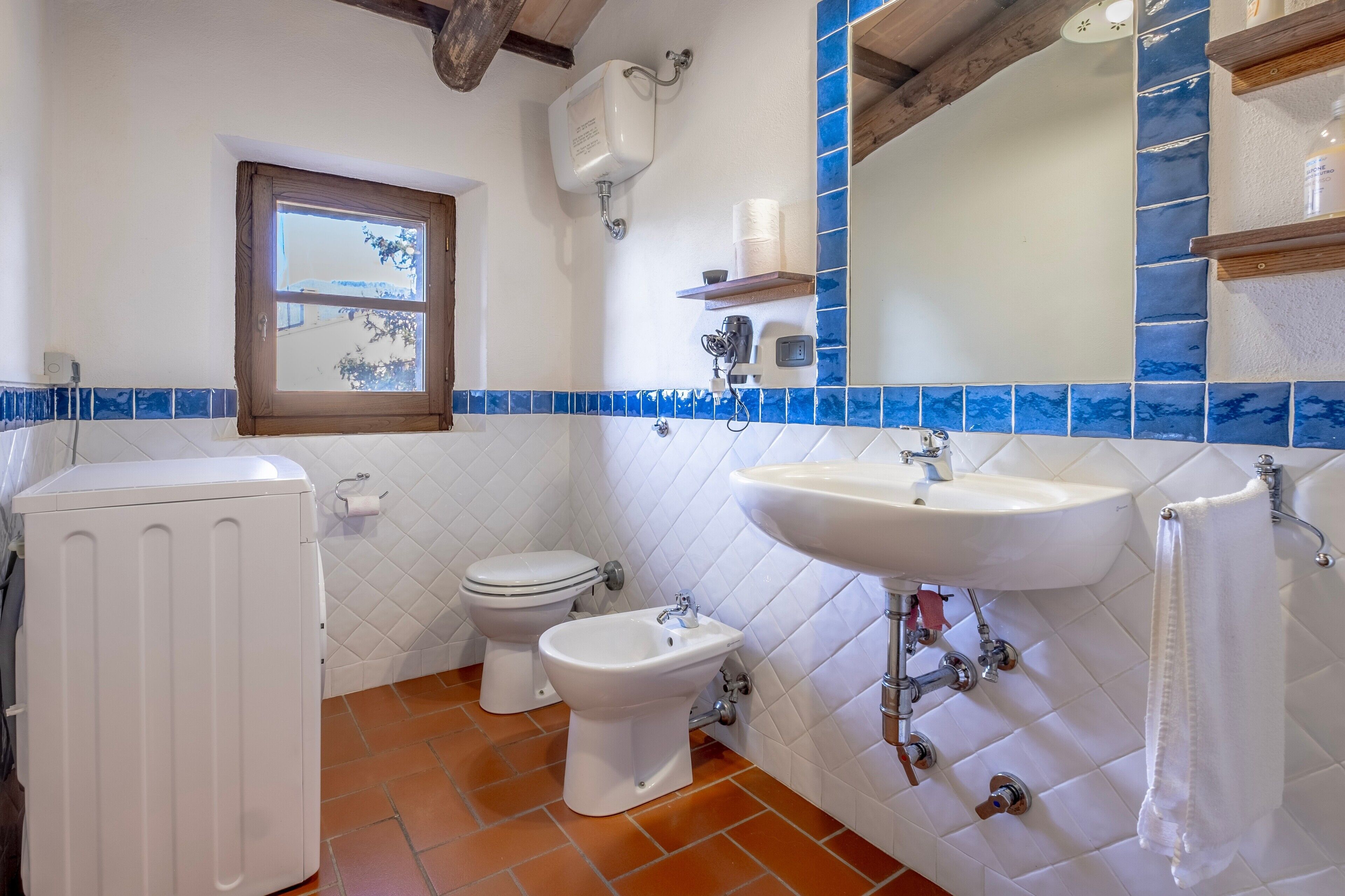Une salle de bain avec des toilettes, un bidet, un lavabo blanc et une fenêtre.