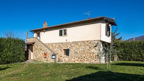 A stone house with a tiled roof, a staircase, and a small garden.