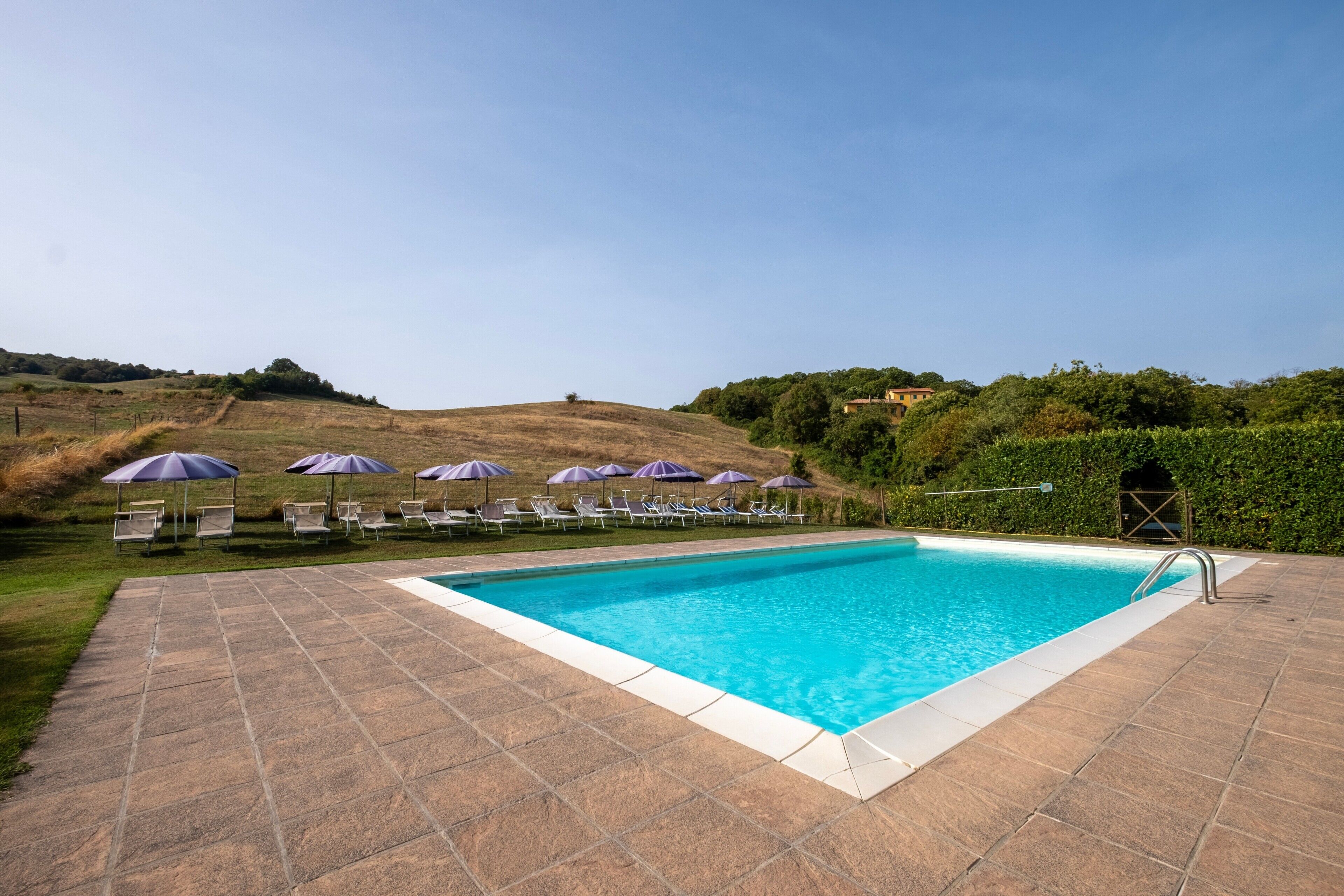 A rectangular swimming pool with a tiled deck, surrounded by lounge chairs and umbrellas.